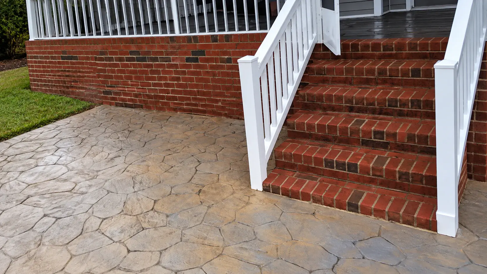 Brick front steps with white railings above a stone patio
