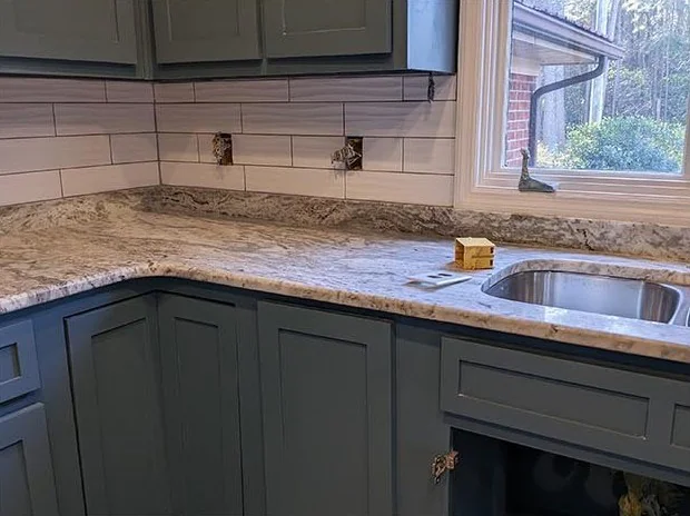 Kitchen corner with gray-blue cabinets, stone counters and a tile backsplash